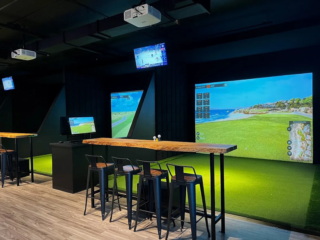 Les baies Trackman d’OB Golf, tables de bois et tabourets face aux écrans.